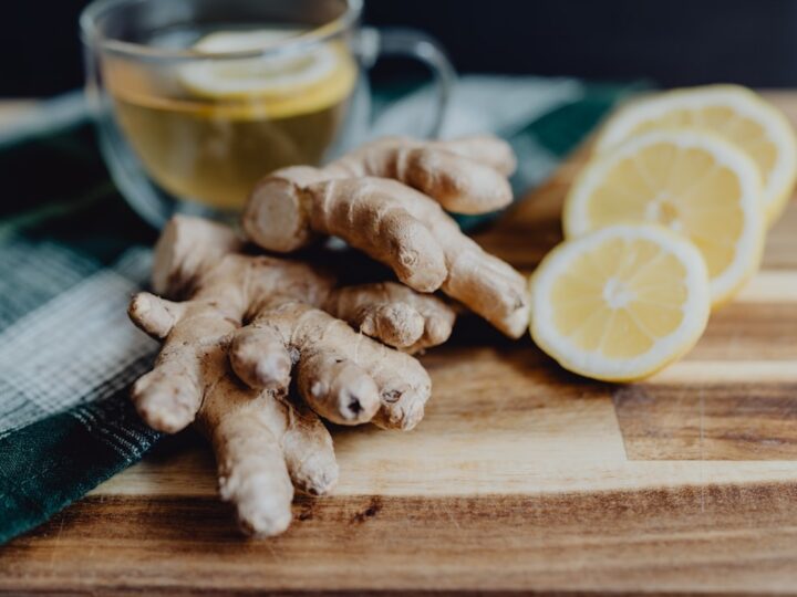A warm clay tumbler of water beside a small brass plate with ginger and rock salt on a wooden kitchen table