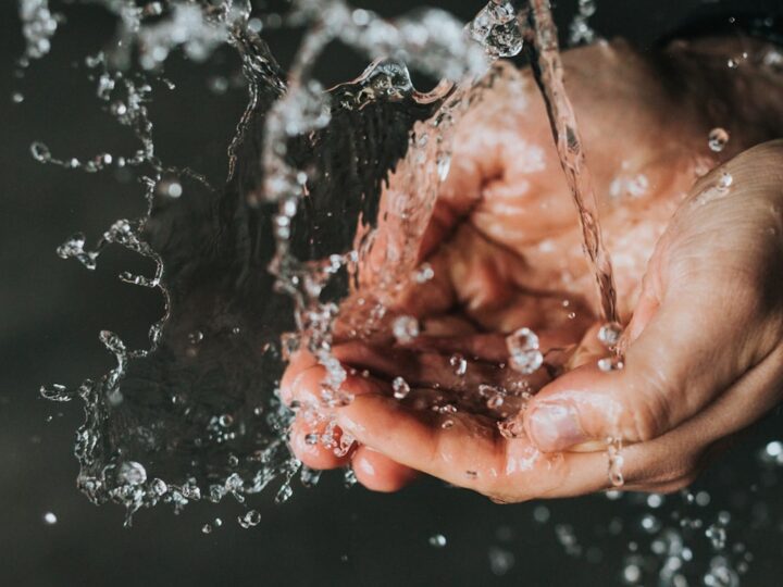 Hands cupping cold water at a ceramic basin in early morning light