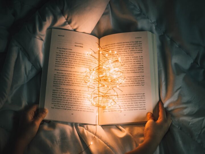 A warm lamp beside an open cloth-bound book on a wooden evening table
